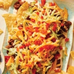 Taco dip on a platter with chips and beer on the side.