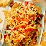 Taco dip on a platter with chips and beer on the side.