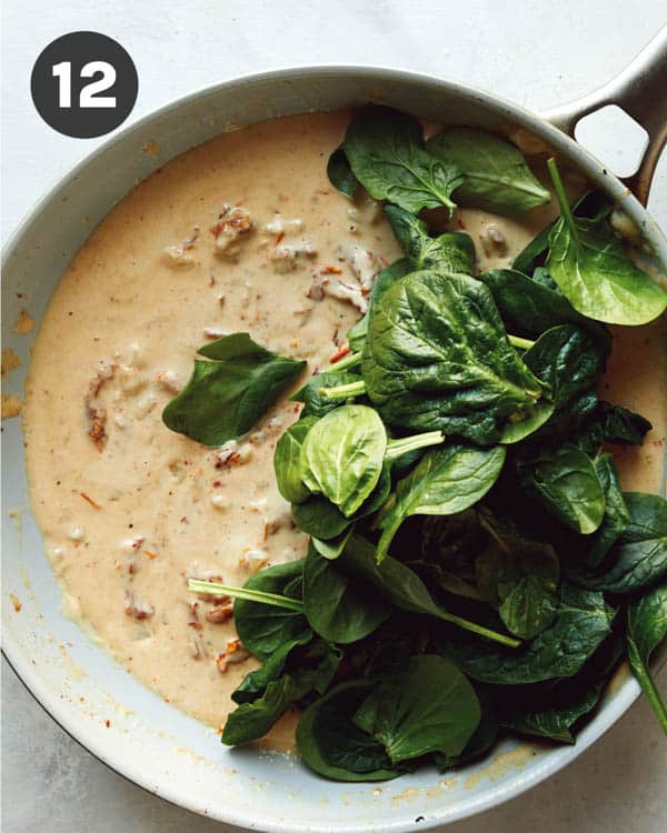 Adding spinach to tuscan chicken sauce in a skillet.