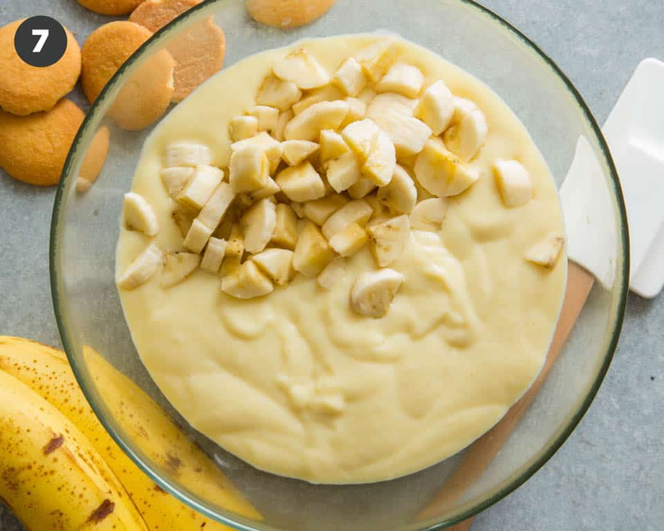 Banana pudding being folded with chunks of bananas. 