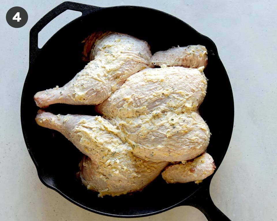 A spatchcock chicken covered in butter in a skillet.