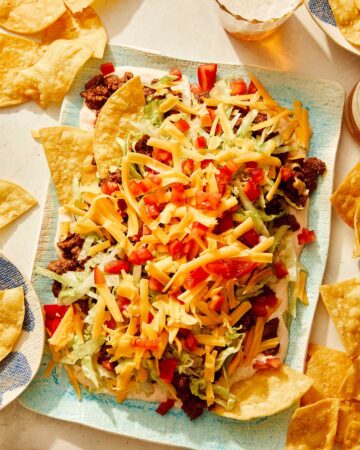 Taco dip on a platter with chips and beer on the side.