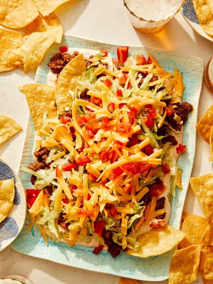 Taco dip on a platter with chips and beer on the side.