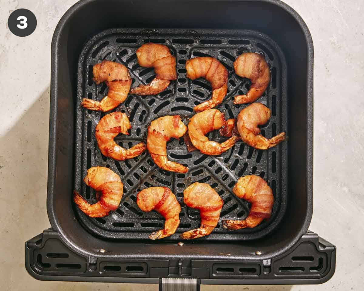 Air fryer shrimp wrapped in bacon cooked in an air fryer basket. 