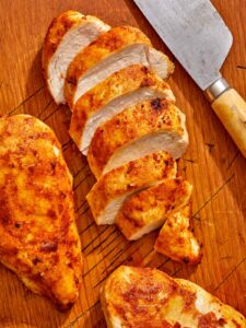 Air fryer chicken breast on a cutting board with a knife.