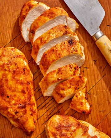 Air fryer chicken breast on a cutting board with a knife.