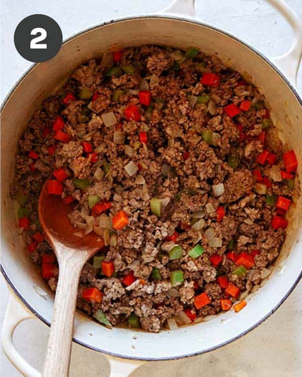 Beef, pork, and italian sausage in a pot with onions and celery to make bolognese sauce.