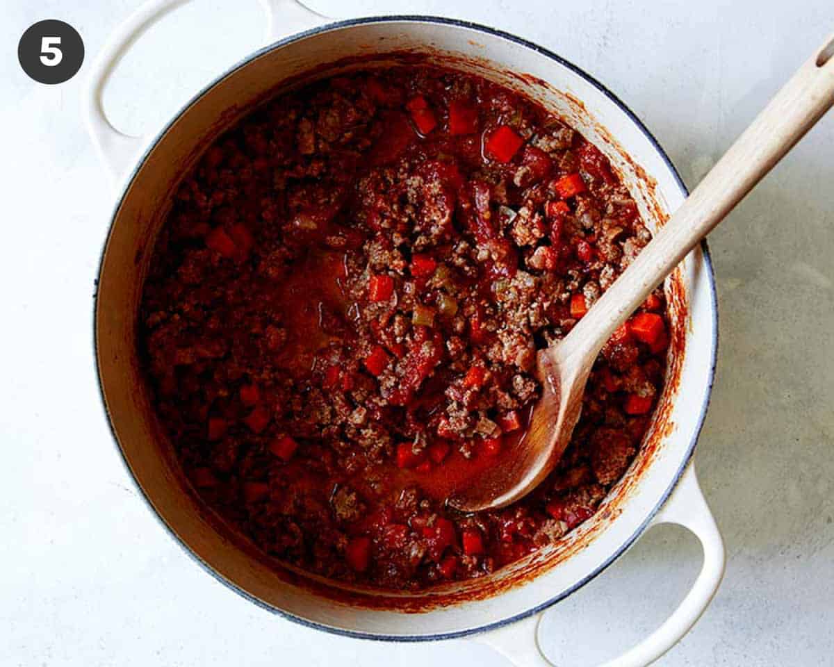 A big pot of bolognese sauce with a wooden spoon in it.