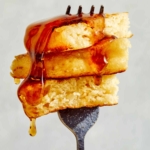 Buttermilk pancake bite on a fork with syrup poured over it.