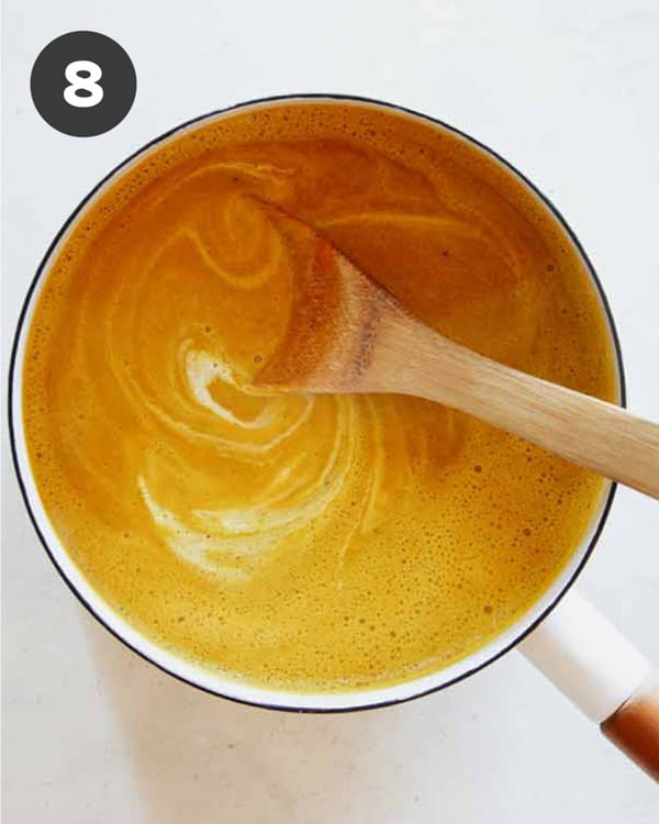 Pumpkin Soup in a stock pot with cream mixed in with a wooden spoon.