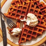 Pumpkin waffles on a plate with whipped cream on top.
