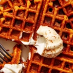 Pumpkin waffles on a plate with whipped cream on top.