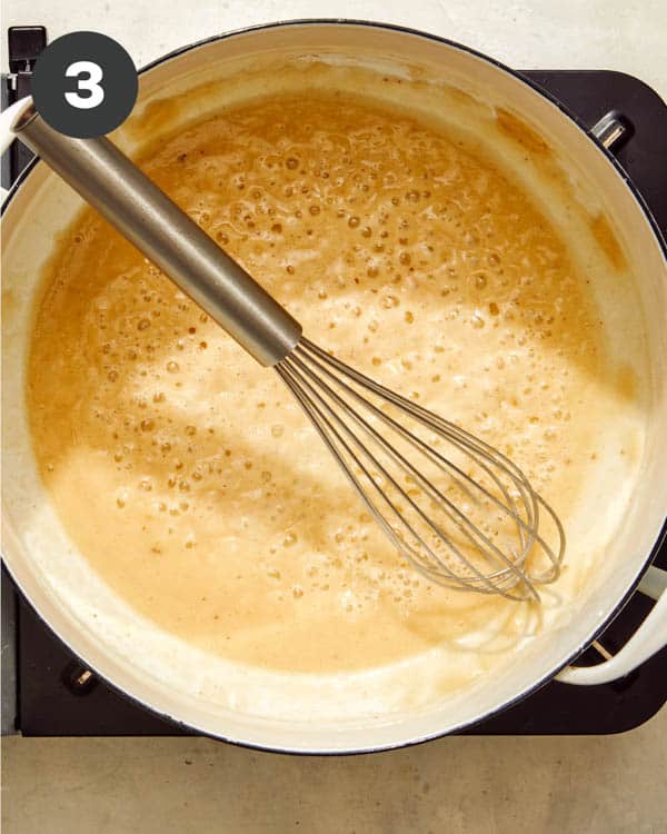 Milk cooking in a pot with flour to make a roux for baked mac and cheese. 
