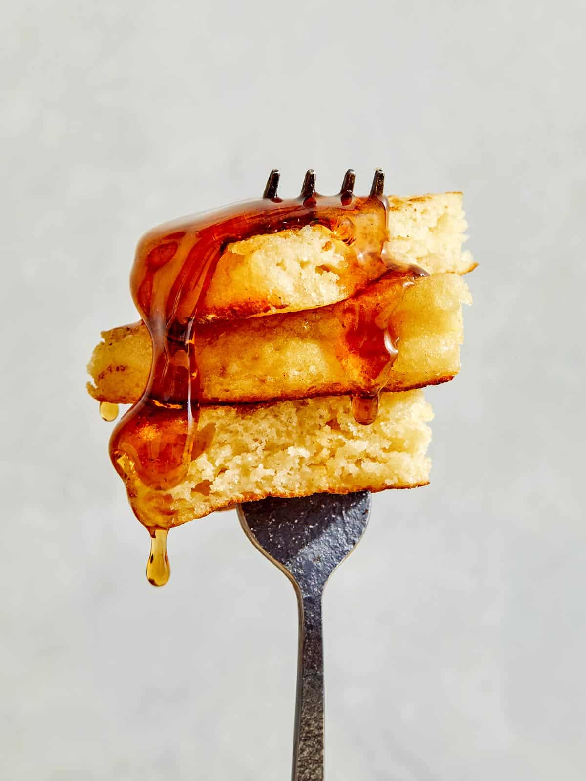 Buttermilk pancake bite on a fork with syrup poured over it. 