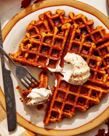 Pumpkin waffles on a plate with whipped cream on top.