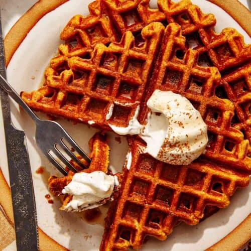 Pumpkin waffles on a plate with whipped cream on top.