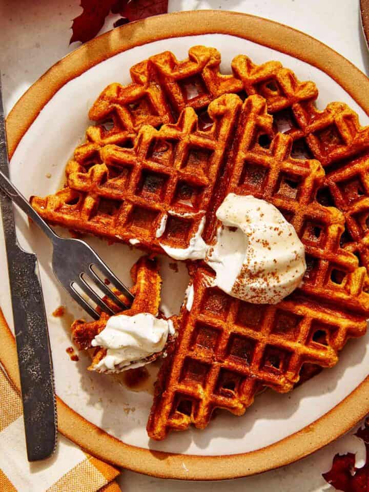 Pumpkin waffles on a plate with whipped cream on top.