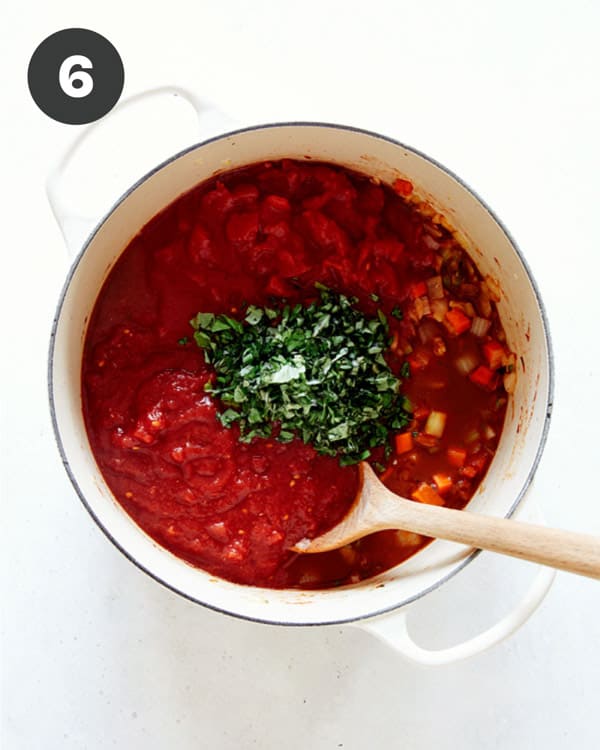 Veg with broth and tomatoes with herbs in a stock pot.