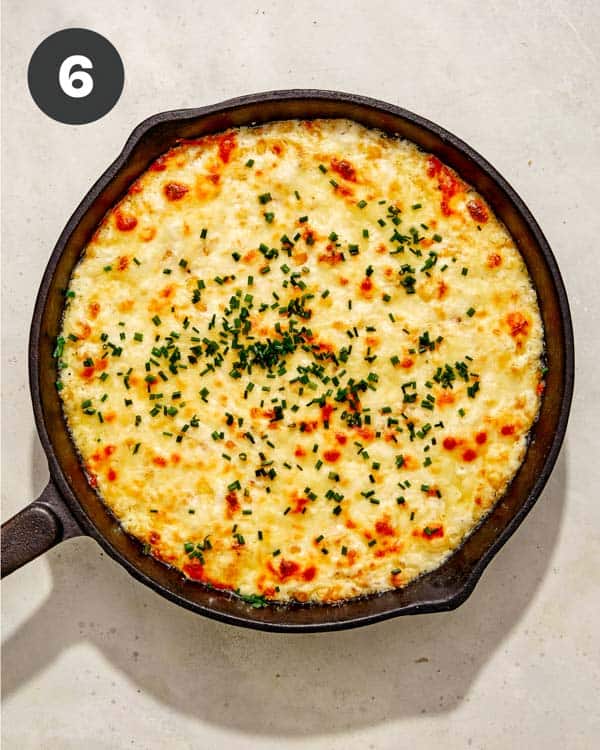 Corn dip in a skillet with chives on top. 