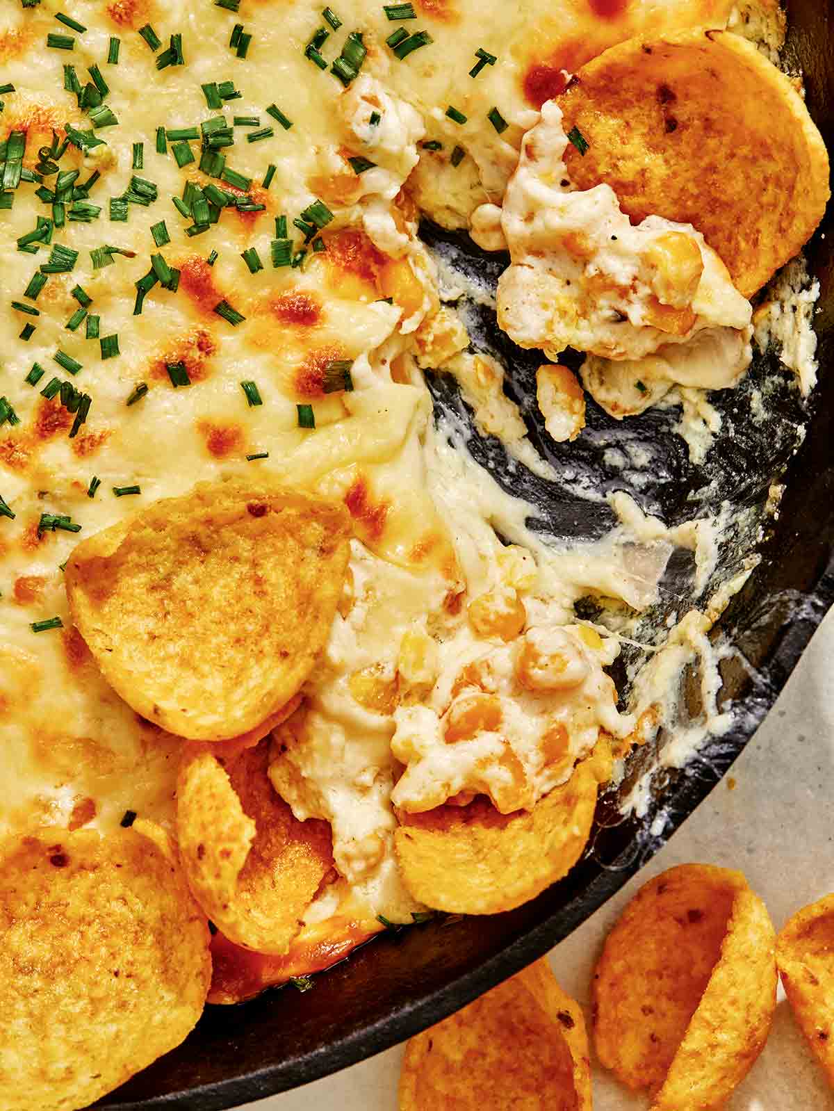 Corn dip close up with chips being dipped into it. 