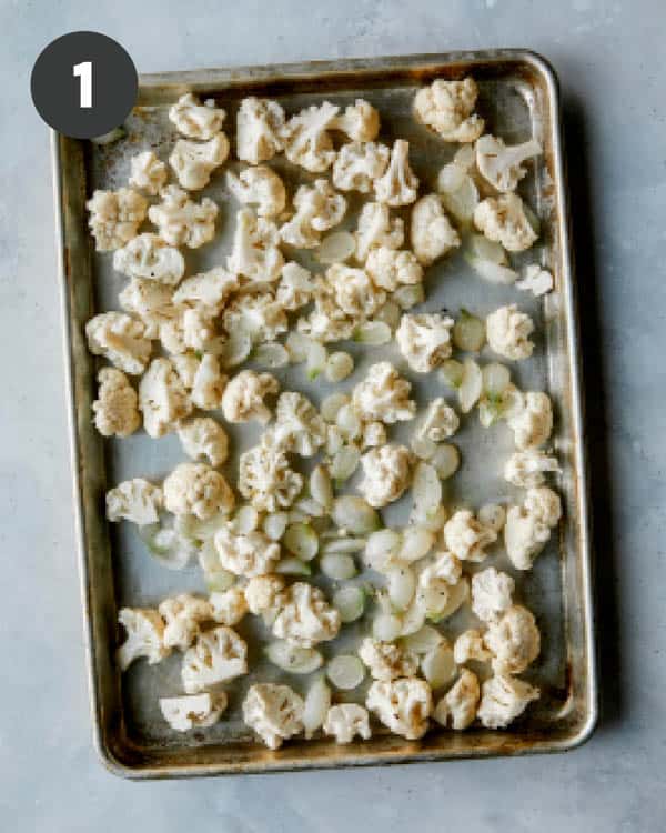 Cauliflower and pearled onions on a baking sheet.
