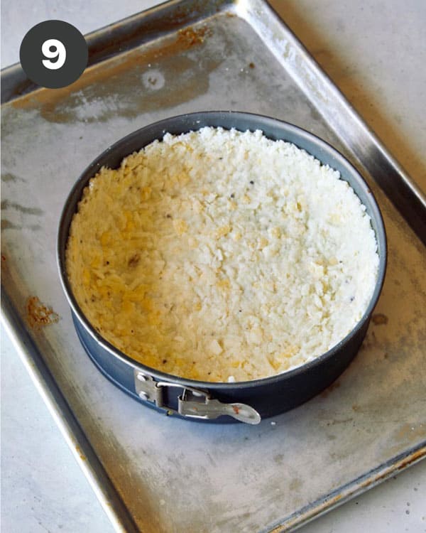A spring form pan filled with a hash brown crust on a baking sheet.