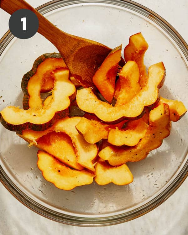 Acorn squash in a bowl with oil and seasoning mixed together.