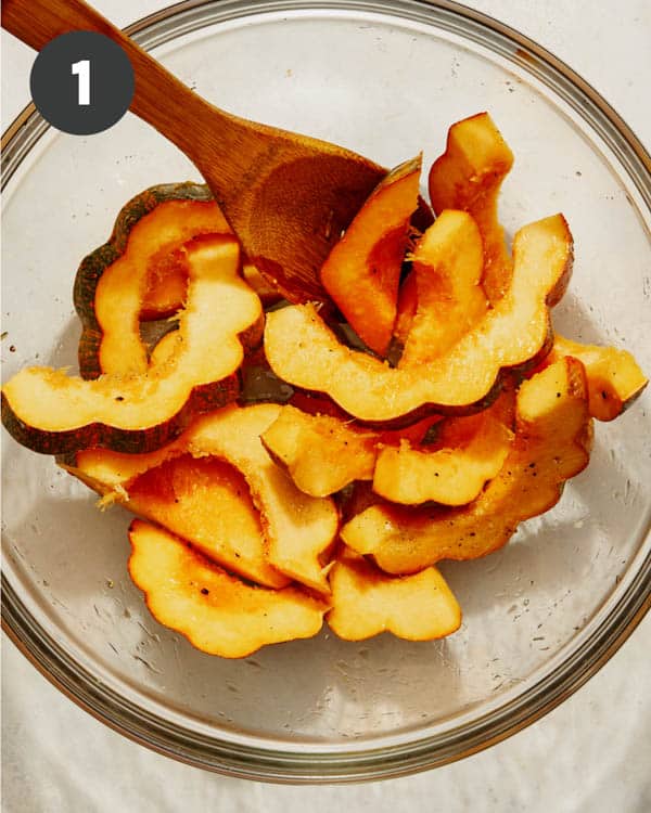 Acorn squash in a bowl with oil and seasoning mixed together. 