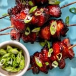 Air fryer chicken skewers with green onions on top.