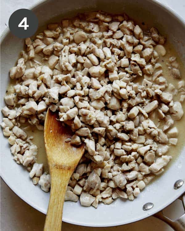 Diced chicken thighs in a skillet cooking.