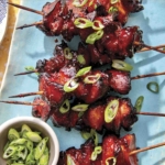 Air fryer chicken skewers with green onions on top.
