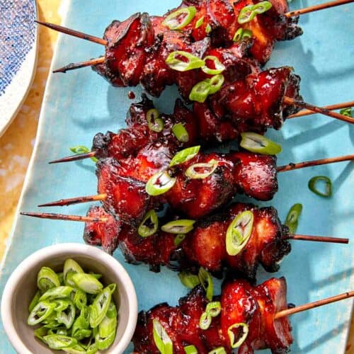 Air fryer chicken skewers on a platter with green onions on top.