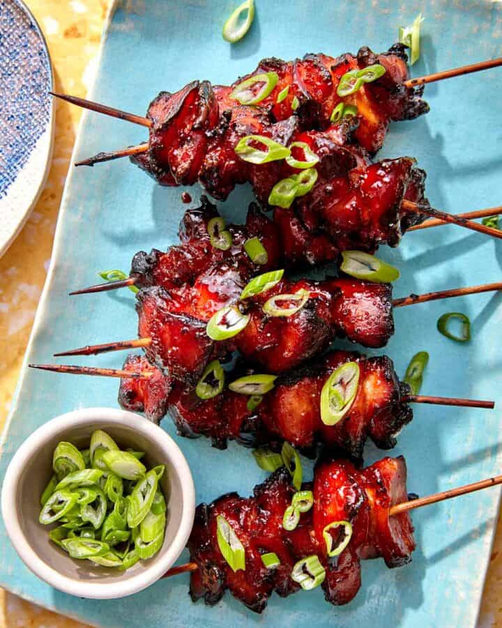 Air fryer chicken skewers on a platter with green onions on top.