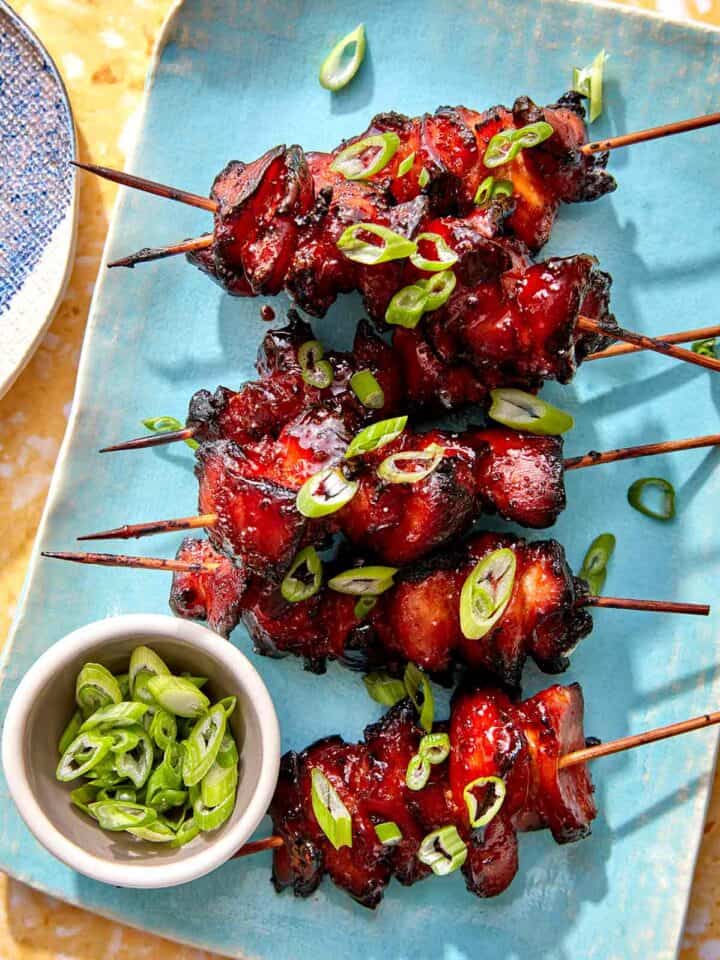 Air fryer chicken skewers on a platter with green onions on top.