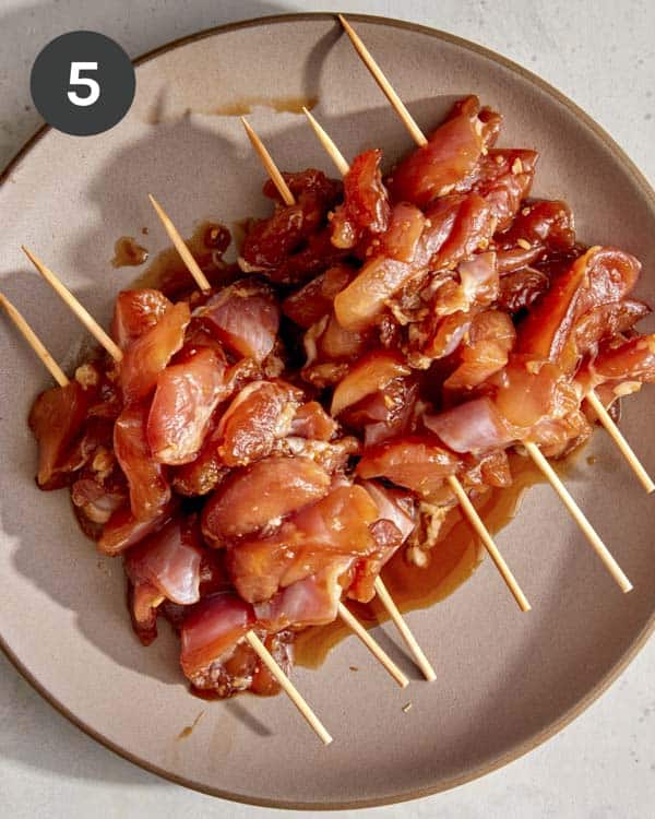 Chicken thighs on skewers with marinade on them.