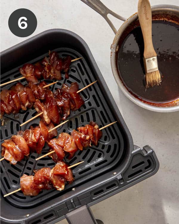 Chicken skewers cooking in a air fryer being brushed with glaze.