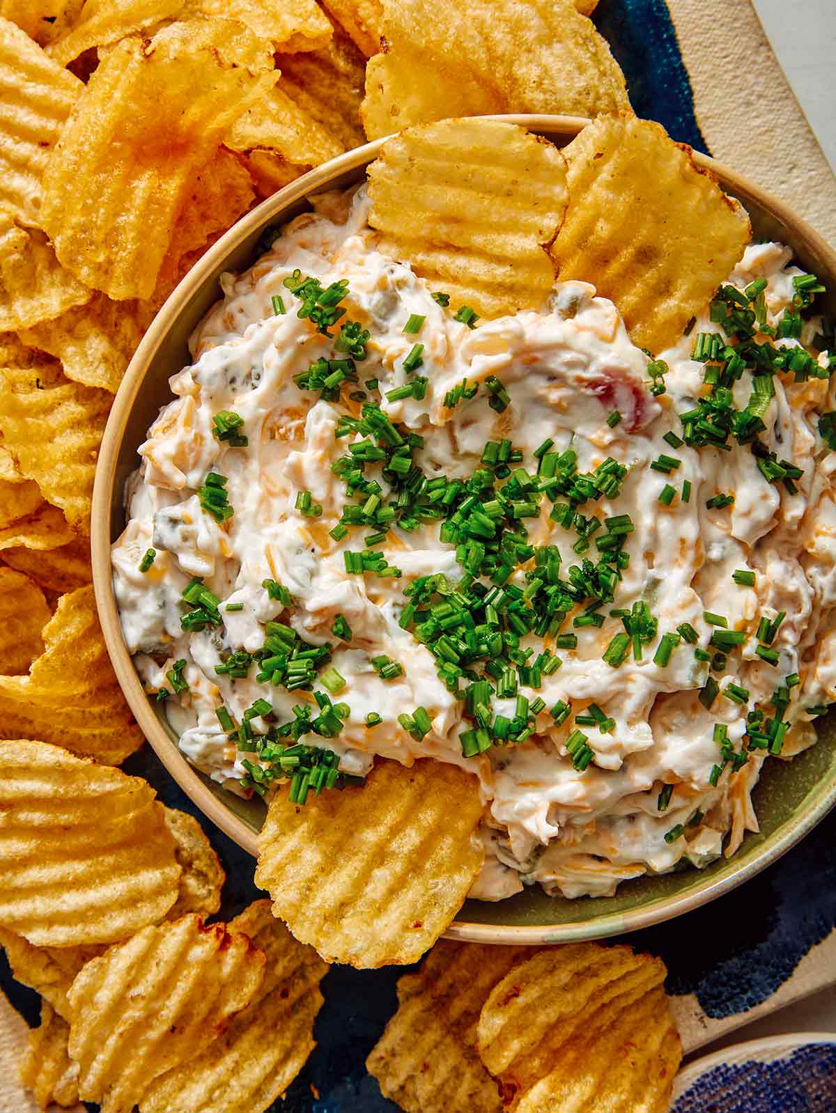 Baked potato dip in a bowl with some potato chips dipped in it.