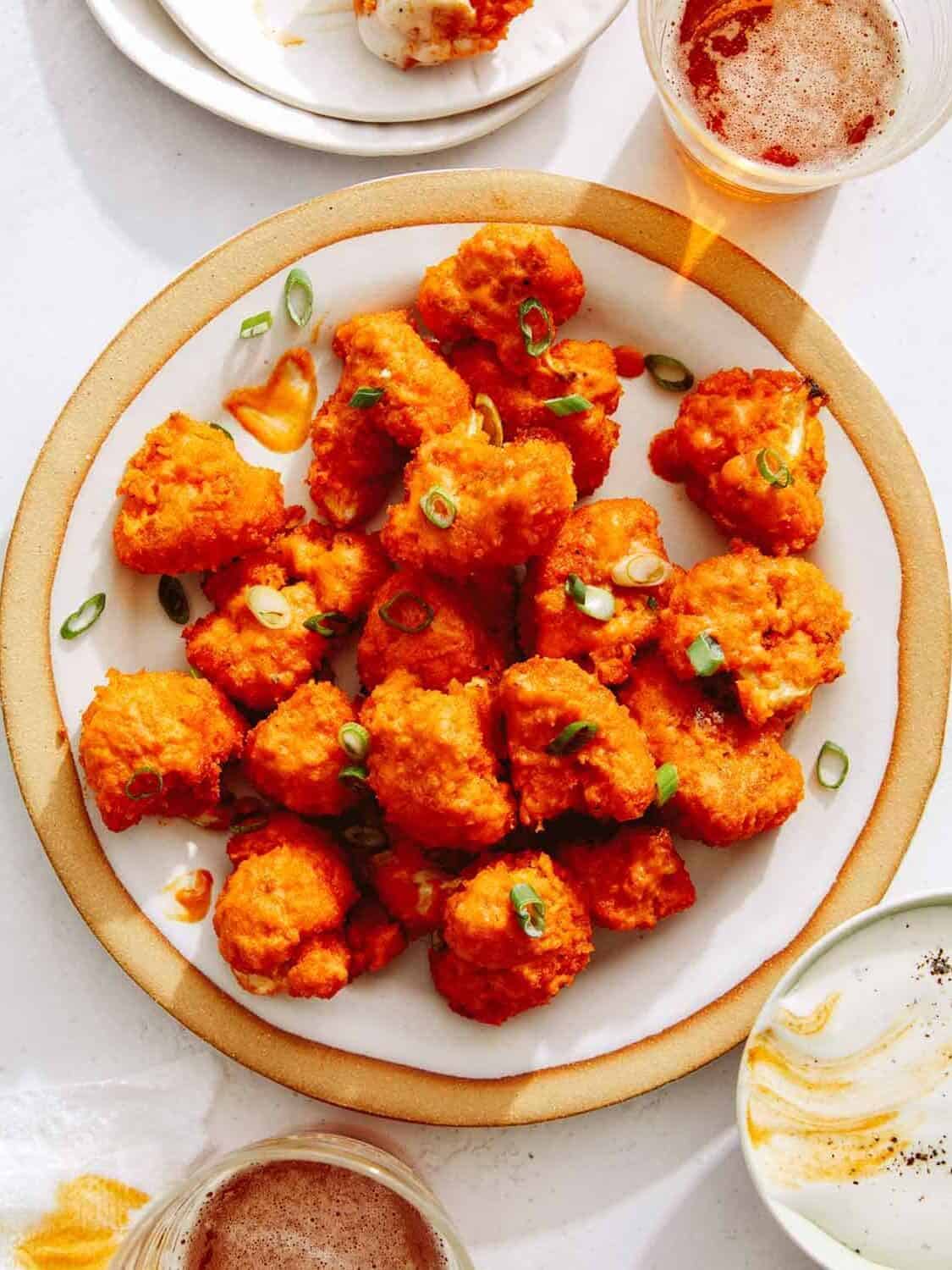 Buffalo cauliflower recipe on a plate with beers next to it, a Super Bowl finger food idea. 