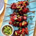 Air fryer chicken skewers with green onions on top.