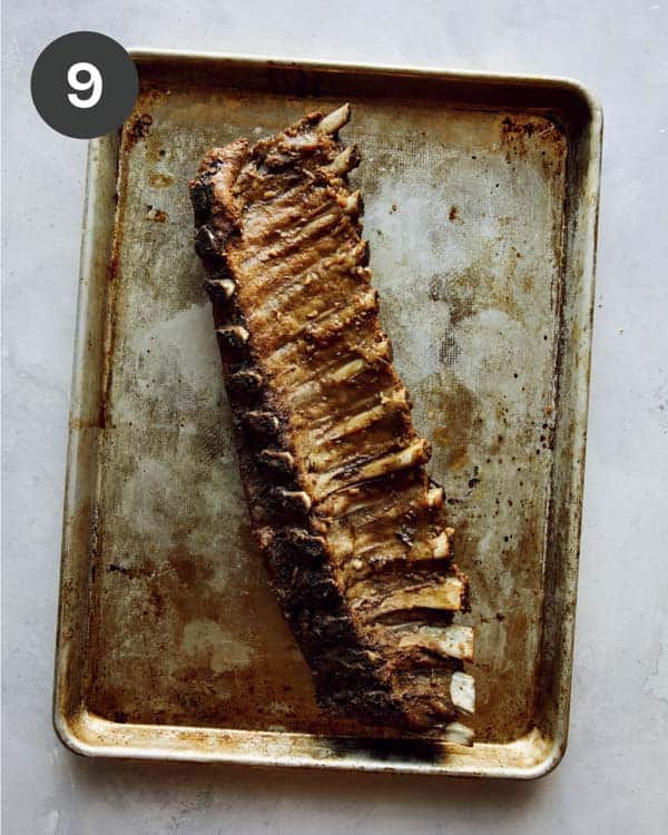 Oven baked ribs on a baking sheet ready to have sauce brushed on top.