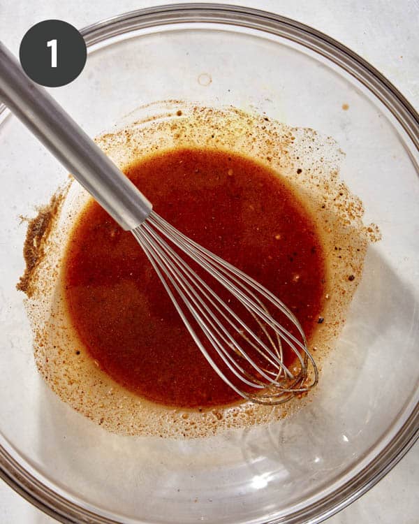Oil and seasonings being whisked together in a glass bowl. 