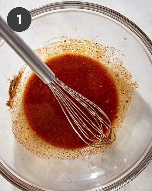 Oil and seasonings being whisked together in a glass bowl.