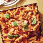 Baked ziti in a baking dish with some scooped out next to it.