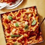 Baked ziti in a baking dish with some scooped out next to it.