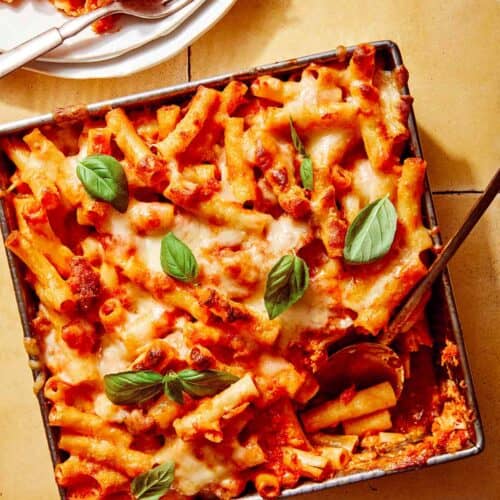 Baked ziti in a baking dish with some scooped out next to it.