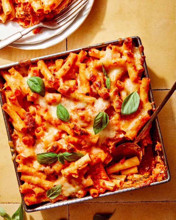 Baked ziti in a baking dish with some scooped out next to it.