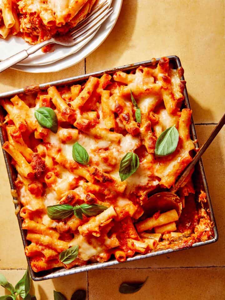 Baked ziti in a baking dish with some scooped out next to it.