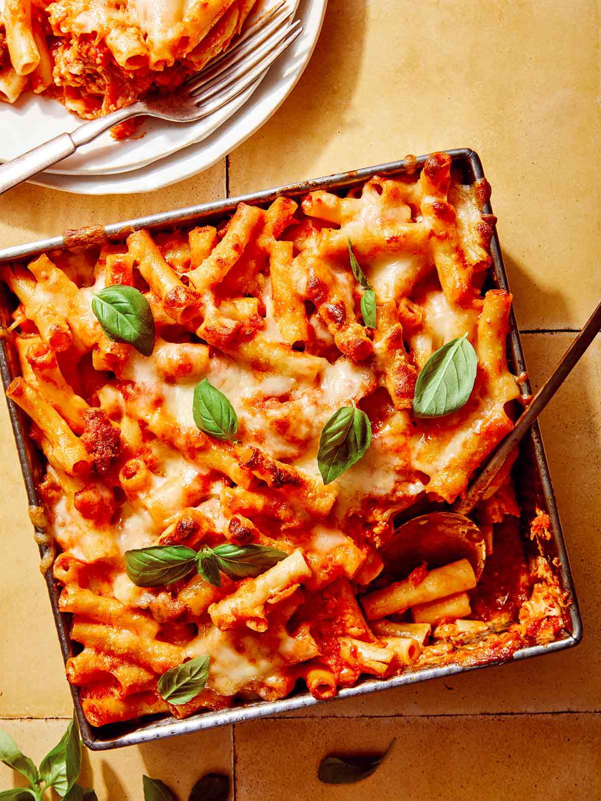 Baked ziti in a baking dish with some scooped out next to it. 