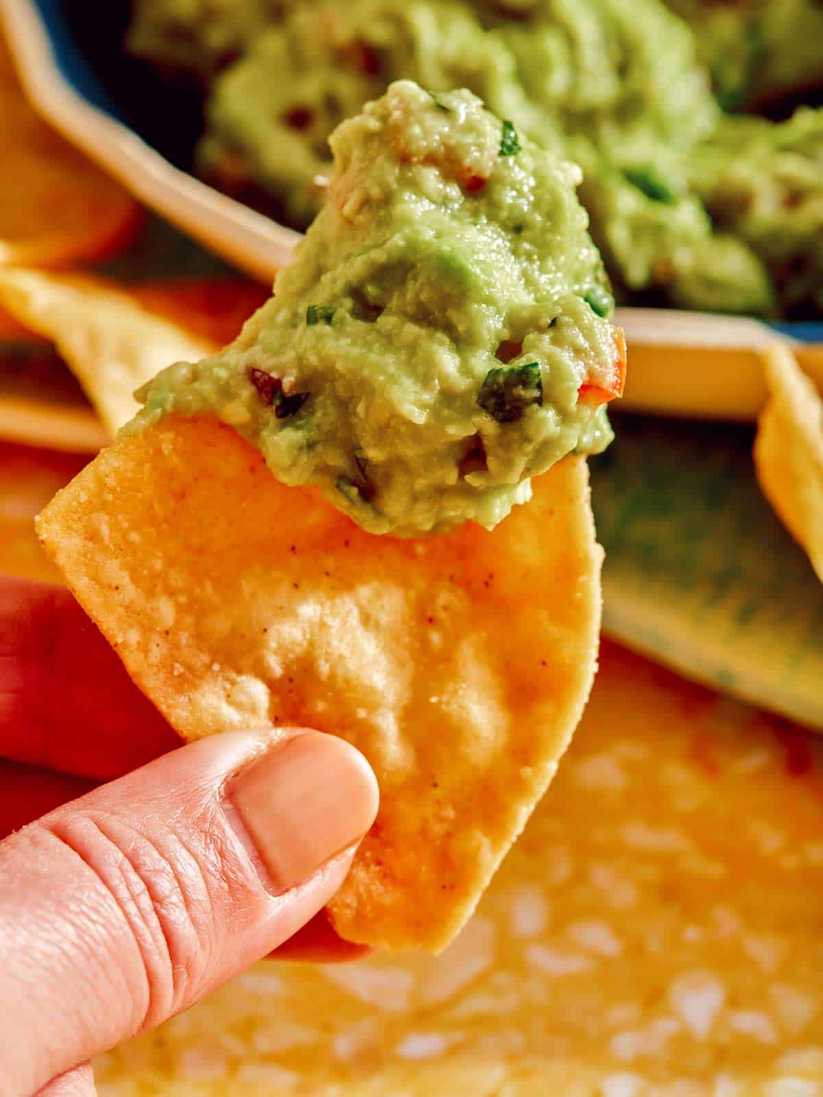 A hand holding up a chip with guacamole on it. 