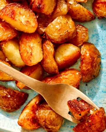 Crispy roasted potatoes on a platter with a fork.